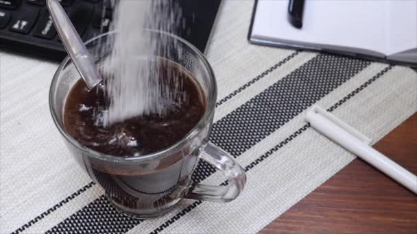 Bílý cukr padá do šálku kávy na pracovním stole s laptopem - Záběry, video