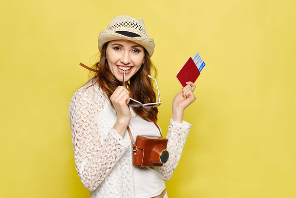 Ein junges Mädchen hält ein Ticket mit Pass und Kamera auf gelbem Hintergrund. Nahaufnahme. - Foto, Bild