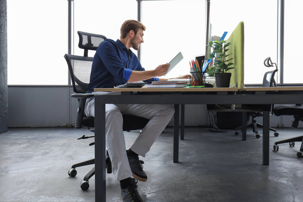 Jeune homme d'affaires moderne travaillant en utilisant une tablette numérique tout en étant assis dans le bureau - Photo, image