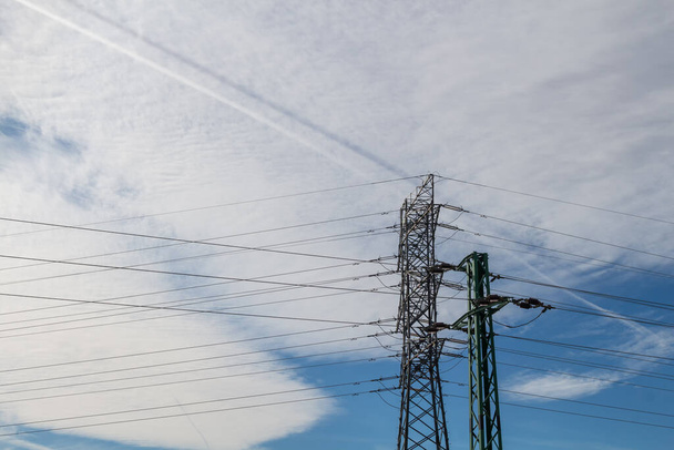 Electricity tower with its cables. Partly bright blue sky, big white cloud. Two trails in the cloud, one white, the other blue. Svaty Jur, Slovakia. - Photo, Image
