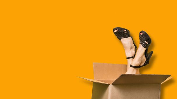 Paketi olan güzel bir kadın, üzerinde bacakları olan karton bir kutu renkli arka plan ve Coronavirus 'a bağlı ticari konsept. - Fotoğraf, Görsel