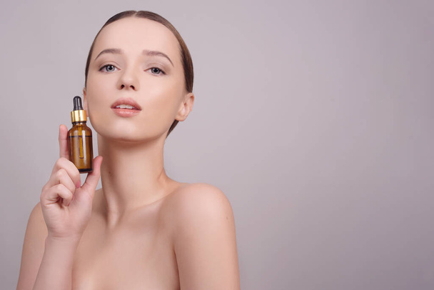 Close-up van model brunette meisje met cosmetische olie op haar gezicht met pipet. Schoonheidstherapie concept. Model met blauwe ogen glimlach, huidverzorging.  - Foto, afbeelding