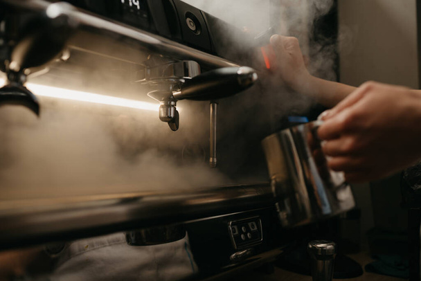 Μια κοντινή φωτογραφία μιας επαγγελματικής καφετιέρας. Ένας μπάρμαν βράζει μια μεταλλική κούπα. - Φωτογραφία, εικόνα