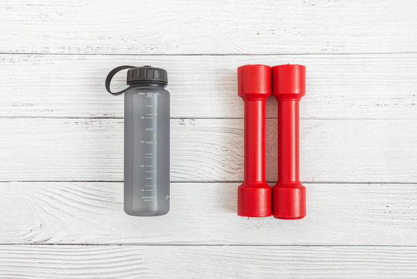 Red dumbbells and water bottle on wooden background. Flat lay composition. Concept of sports, fitness, healthy lifestyle. Top view. - Foto, Imagen