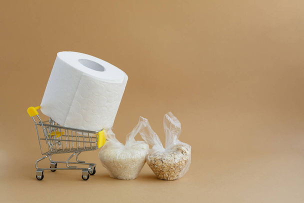 toilet paper in a grocery cart and various cereals in small plastic bags on a brown background. Rice and oatmeal - Foto, afbeelding