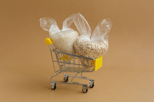 various groats in packages in a grocery cart on a brown background. Rice and oatmeal - Foto, Imagem
