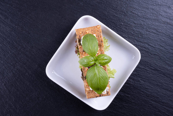 cracker appetizer, basil on a white plate on a black background - Fotoğraf, Görsel