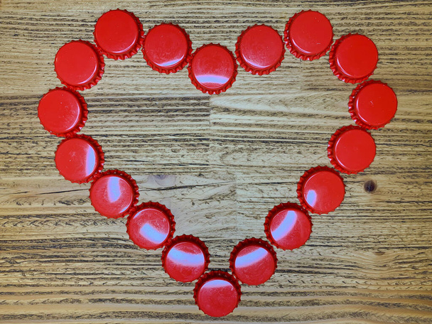 Red love heart made from beer bottle tops lids on a rustic wooden table. Beer drinkers Valentine's day concept, top view horizontal stock image. - Photo, Image
