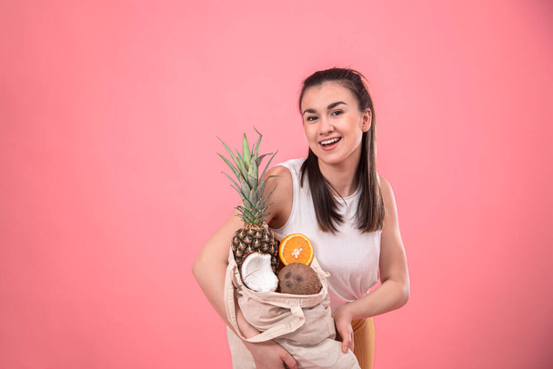 Retrato de una mujer joven y elegante con una bolsa de fruta ecológica sobre un fondo rosa aislado
. - Foto, Imagen