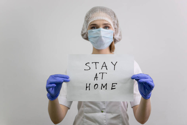 The doctor is holding a sheet with the inscription stay at home. The girl nurse urges people to self-isolate and observe quarantine during the coronavirus pandemic. - Фото, зображення