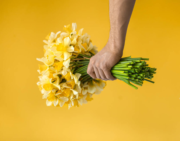 Hipster-a man on a yellow background in a shirt and a large bouquet of daffodils. The concept of greetings and women's day. - Foto, Imagen