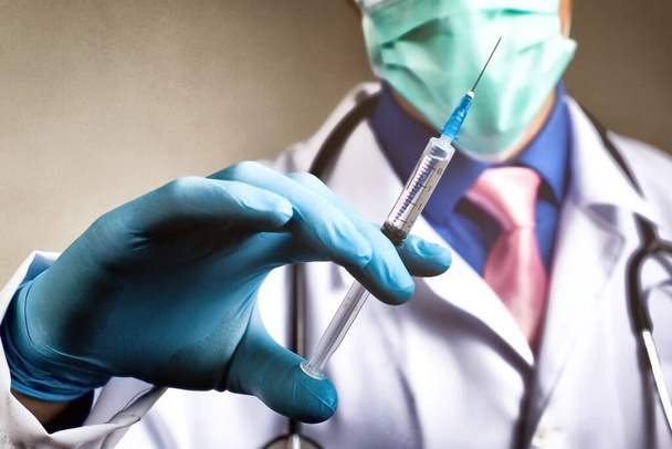 Dokter met gaasmasker en medische badjas met spuit in zijn blauwe rubberen handschoen. Gezondheid en vaccinatie - Foto, afbeelding