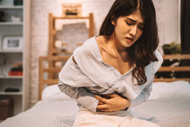 Húszas évekbeli fiatal ázsiai nő portréja, akit fájdalom és fájdalom gyötör a gyomrában egy hálószobában éjszaka. Tünetek, mint például hasmenés, székrekedés, bél, gyomorhurut, menstruáció - Fotó, kép
