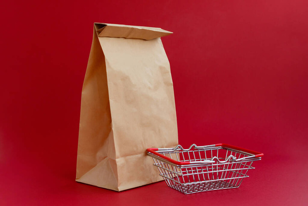brown paper craft bag for shopping on a red background and a small grocery basket - Foto, afbeelding