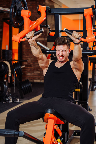 Huge pressure. Half-length portrait of a young European brunette man doing gym with big tension. Strong muscular handsome attractive  bodybuilder is a training workout - Photo, Image