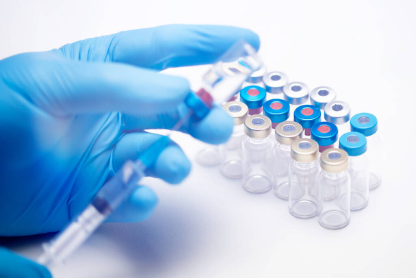Un scientifique porte des gants bleus portant le coronavirus, une maladie vaccinale covid-19, se préparant pour les essais cliniques humains injection de vaccin. Médecine et concept de médicament
 - Photo, image