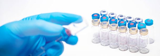 Scientist hand in blue gloves holding coronavirus, covid-19 vaccine disease, preparing for human clinical trials vaccination shot. Medicine and drug concept - Photo, image