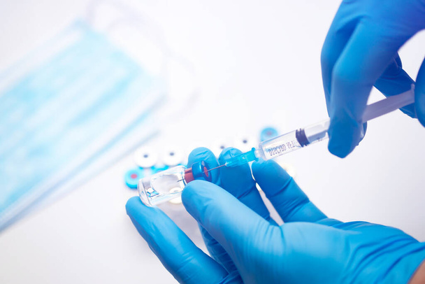 Scientist hand in blue gloves holding coronavirus, covid-19 vaccine disease, preparing for human clinical trials vaccination shot. Medicine and drug concept - Photo, Image