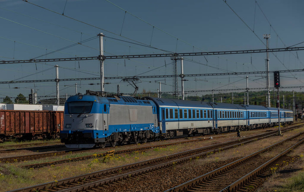 春の暑い日にValasske Mezirici駅で旅客コーチとブルー電気エンジン - 写真・画像