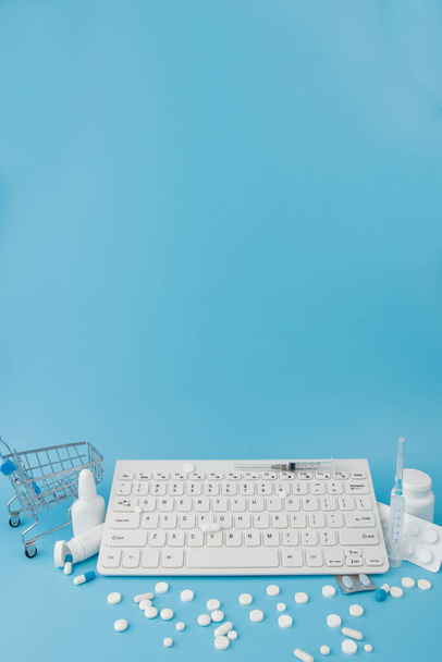 Shopping cart toy with medicaments and Keyboard. Pills, blister packs, medical bottles, thermometer, protective mask on a blue background. . Health care and internet shopping. Top view with place for your text. - Foto, immagini