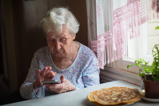 Emeklilerin kendilerini izole etmeleri. Yaşlı bir kadın evinde elinde akıllı bir telefonla oturuyor..  - Fotoğraf, Görsel