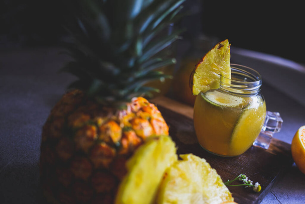 suco de laranja abacaxi com um fundo escuro e suas respectivas frutas de um lado
 - Foto, Imagem