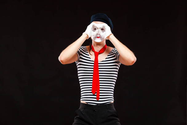 Portrait of male mime artist performing, isolated on black background. Man folds his hands as if looking through binoculars - Photo, image
