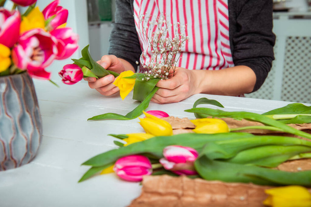 Bez twarzy młody człowiek robi wiosenny bukiet używając tulipanów. Online samokształcenie kwiaciarstwa. Uczę się układania kwiatów. Dostawa kwiatów. Mężczyzna kwiaciarnia tworząc porządek. Skupienie selektywne - Zdjęcie, obraz