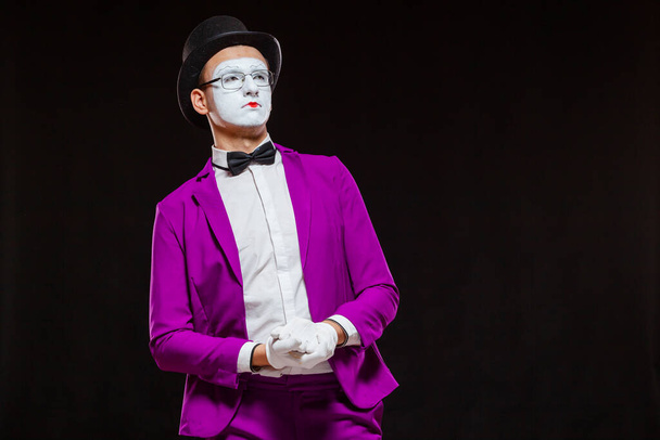 Portrait of male mime artist, isolated on black background. Young man in purple suit is touching his chin with a thoughtful look. Symbol of reflection, criticism - Фото, изображение