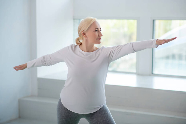 Mature blonde female standing in warrior pose with arms parallel to the floor - Фото, зображення