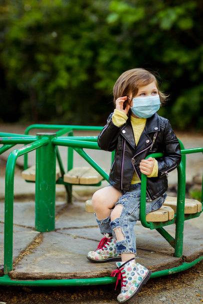 little cool girl, walking in the Playground, wearing a medical mask, during quarantine, because of the covid-19 pandemic - 写真・画像