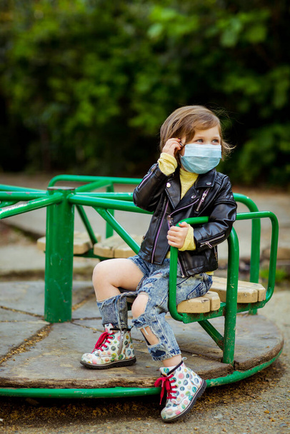 little cool girl, walking in the Playground, wearing a medical mask, during quarantine, because of the covid-19 pandemic - Foto, Imagem