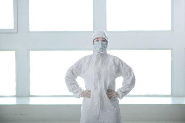 Медичний працівник в захисному одязі, медична маска та окуляри, що стоять з руками на талії
 - Фото, зображення