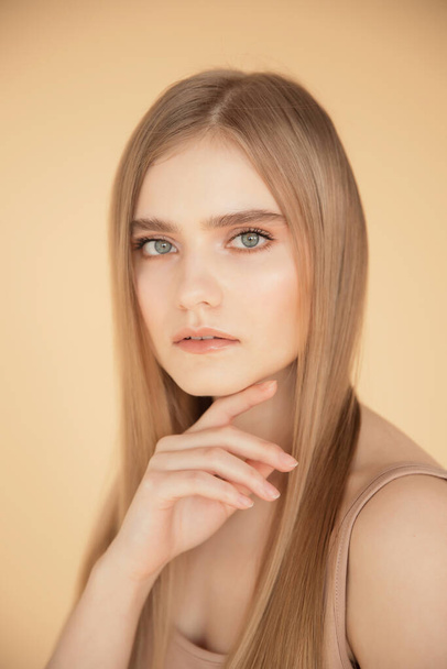 Vertical portrait of beautiful young blonde girl with clean skin, holds hand near face, beige background. Beauty care fashion concept - Fotografie, Obrázek
