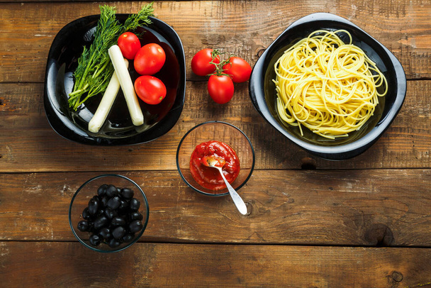 Black plate with pasta and vegetables to decorate Italian dishes on a wooden table. - Foto, Imagem