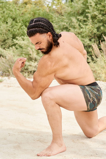 młody muskularny mężczyzna ćwiczący na plaży, młody muskularny mężczyzna ćwiczący kulturystykę na plaży, wysportowany młody mężczyzna pozujący na plaży - Zdjęcie, obraz