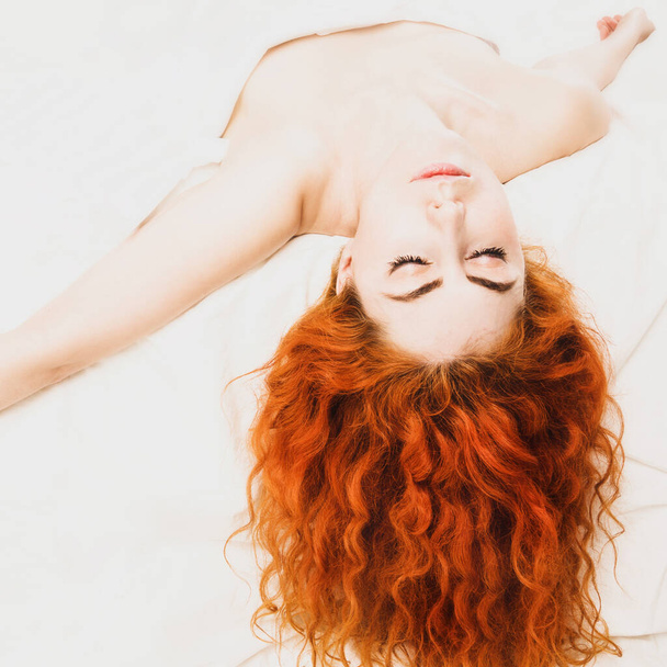 Όμορφη κοκκινομάλλα γυναίκα ξαπλωμένη στο κρεβάτι στην κρεβατοκάμαρα.  - Φωτογραφία, εικόνα