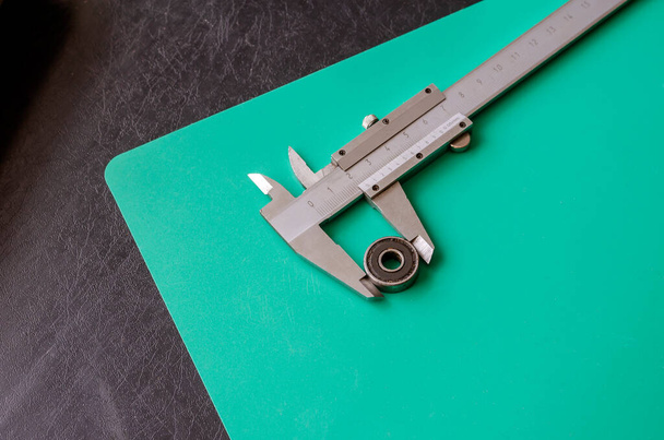 Ball bearing and vernier caliper on a black and turquoise background. Metal vernier caliper with decimal measurement system. Calculation of the dimensions of the old bearing for replacement. - Photo, Image