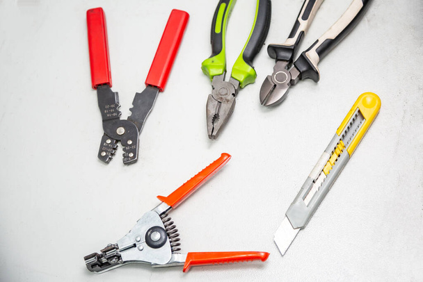 Tools for electrical installation on a white background. In the foreground a stripper for stripping wires. Tool for crimping wires, pliers, wire cutters, segment knife. Horizontal orientation. - Foto, Imagen