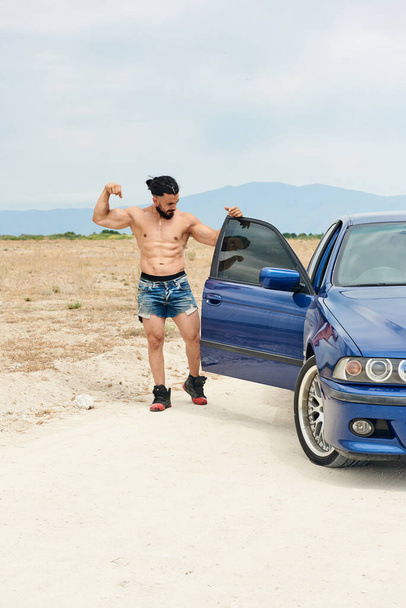 jeune homme de sport posant près de la voiture de sport bleue sur la plage
 - Photo, image