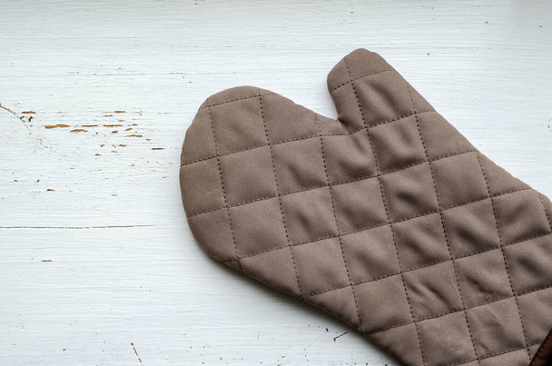 Brown kitchen quilted glove on a white wooden background. Wooden background with cracked paint. Place for text. View from above. - Fotoğraf, Görsel