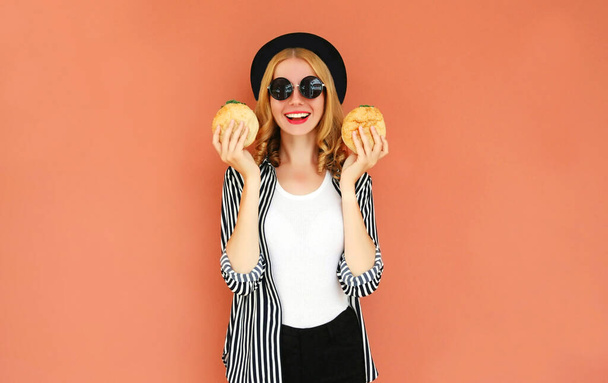 Portrait smiling young woman showing a burger wearing a black hat, sunglasses over wall background - Foto, immagini