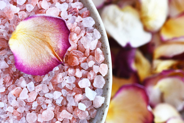 A close up image of pink Himalayan bath salt with yellow and red dried rose petals.  - 写真・画像