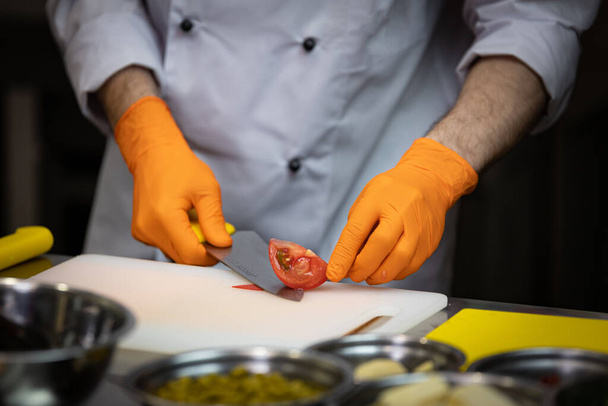 Kokki poistaa ihon veitsellä tomaatista, leikkuulaudalla, keittiössä
 - Valokuva, kuva