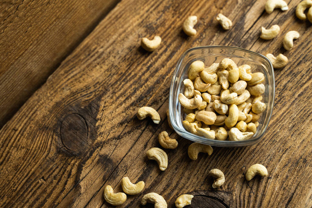 Cashew nuts in a small plate with scattered cashew around a plate on a vintage wooden table as a background. Cashew nut is a healthy vegetarian protein nutritious food. - 写真・画像