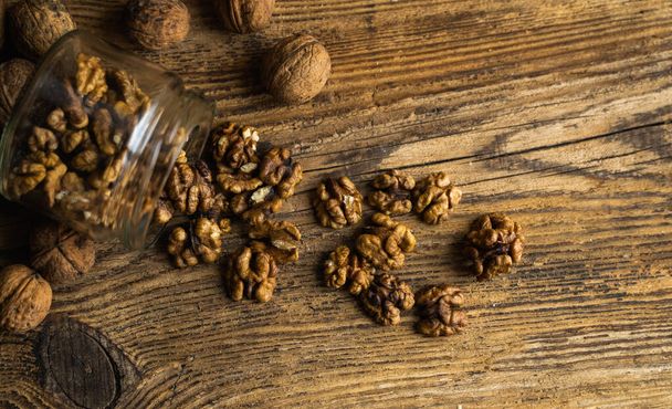 Walnut scattered on the vintage table from a jar whith a whole walnuts. Walnut is a healthy vegetarian protein nutritious food. Walnut kernels and whole walnuts on rustic old wood. - 写真・画像