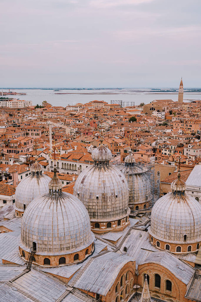 Vista superior da Catedral de St. Marks, na Praça St. Marks, com uma grande torre de tijolos. Contra o pano de fundo dos telhados laranja azulejos da cidade velha de Veneza, na Itália
. - Foto, Imagem
