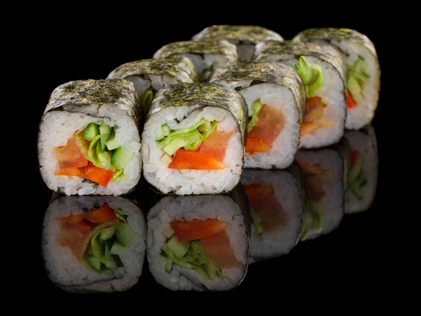 Vegetarische Sushi-Rolle mit Gemüse: Paprika, Gurken, Avocado und Salat isoliert auf schwarzem Hintergrund mit Spiegelung - Foto, Bild
