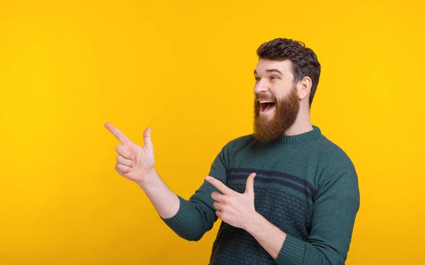 Aufgeregter Mann zeigt mit beiden Händen zur Seite auf gelben Hintergrund. - Foto, Bild