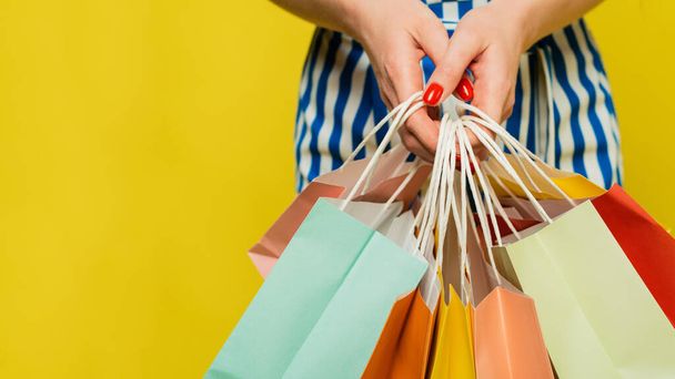 A woman holds different colored bags with groceries, clothes and various purchases in her hands with fresh red manicure. The concept of shopping, shopping and sale. Close up. Web banner - Foto, imagen